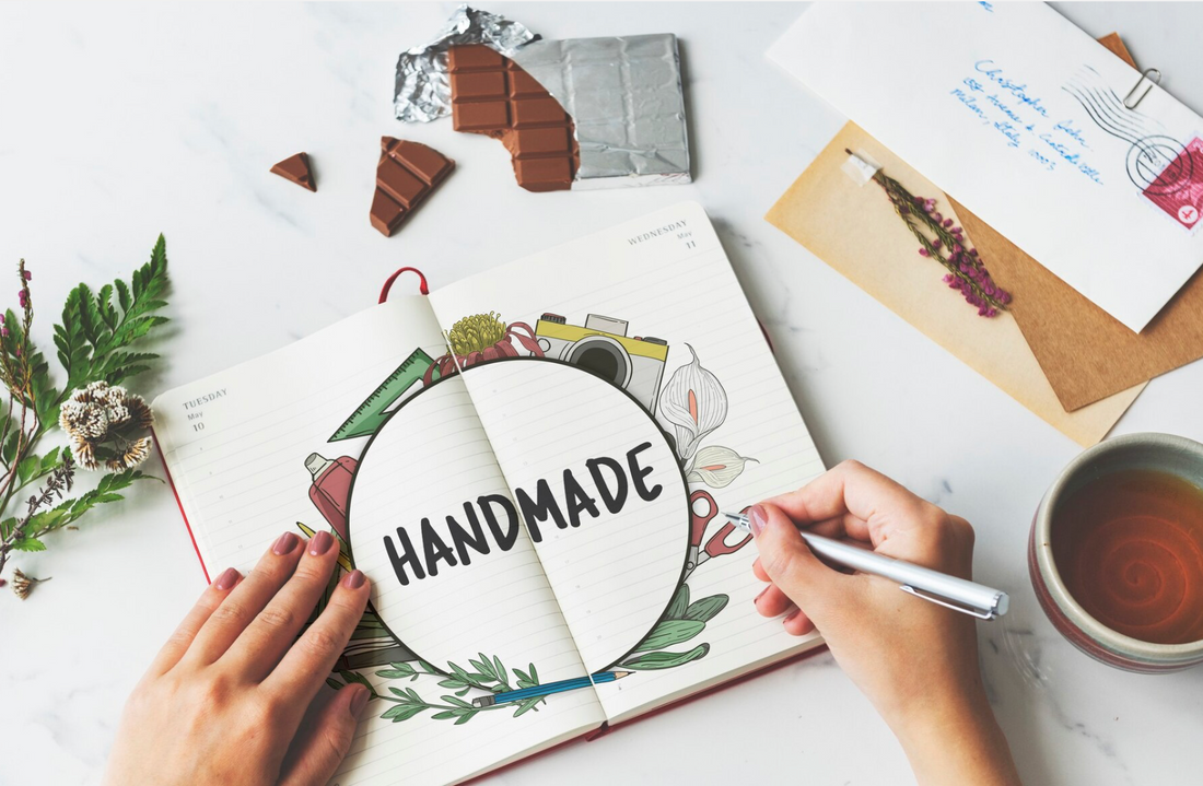 Mains qui écrivent sur un cahier le mot "Handmade".