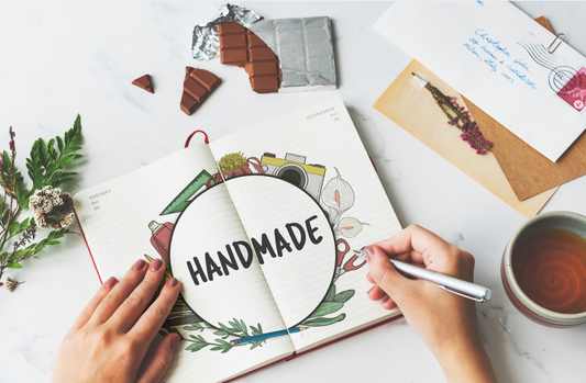 Mains qui écrivent sur un cahier le mot "Handmade".