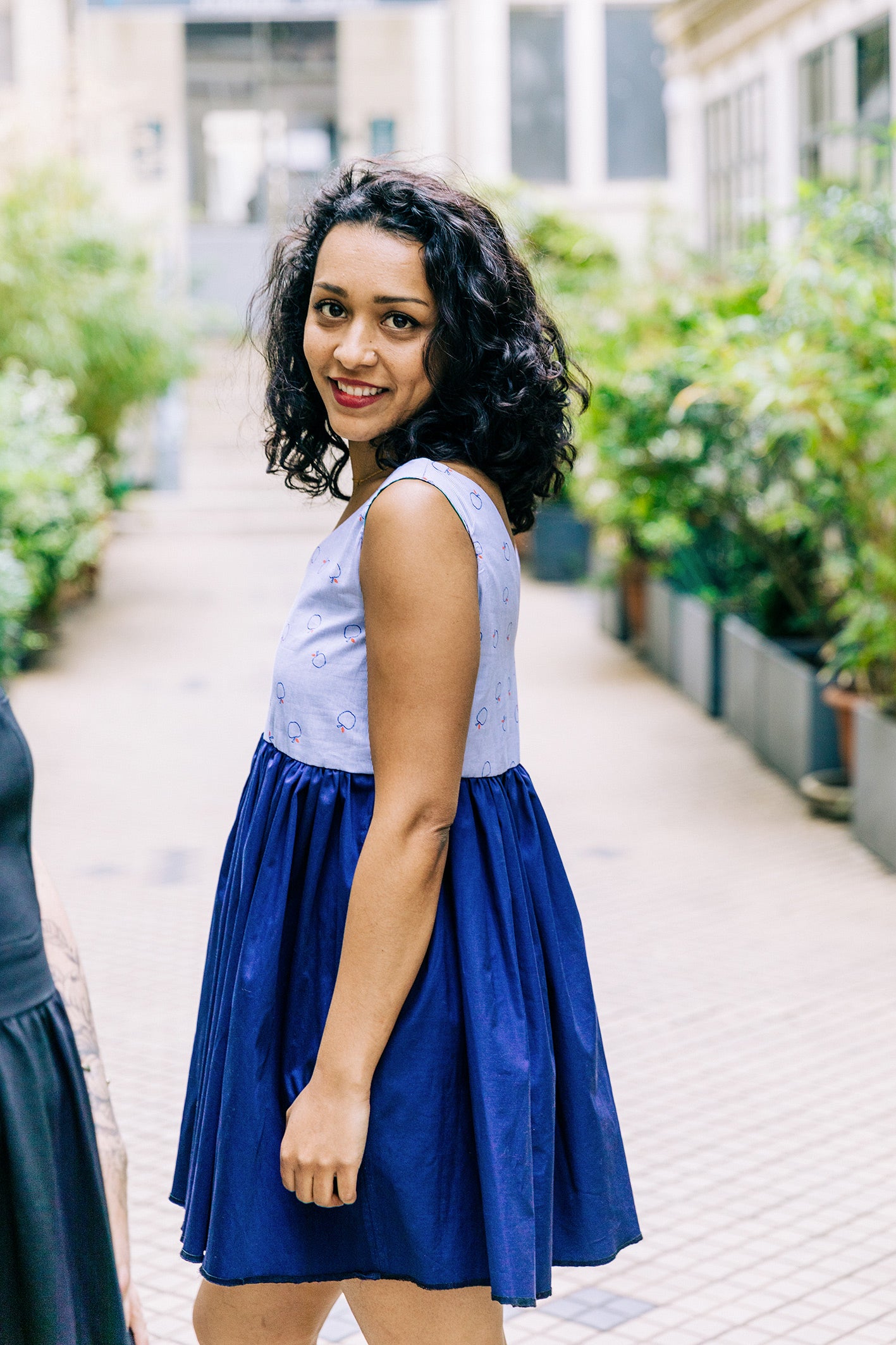 Robe courte en coton deux couleurs : Rayée bleu clair sur le haut de la robe avec des petites pommes rouges sur le haut et un coton bleu marine sur la jupe. La robe est volumineuse ornée de fronces sous poitrine. 