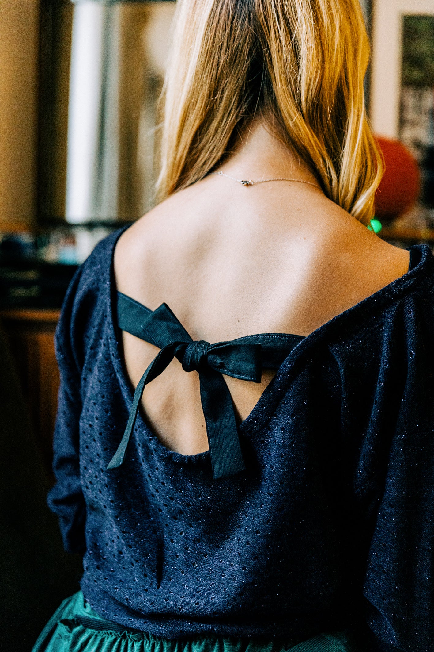 Dos d’un pull élégant en jersey de laine bleu marine, orné d’un décolleté dos nu souligné par un ruban en soie noire noué en nœud. Création sur mesure confectionnée en France dans notre atelier couture à Paris.