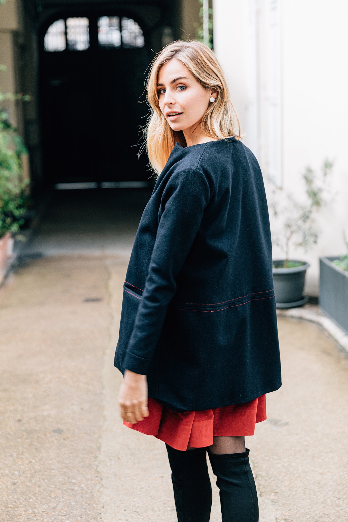 Vue de dos. Manteau court en laine bleu marine et surpiqure rouge